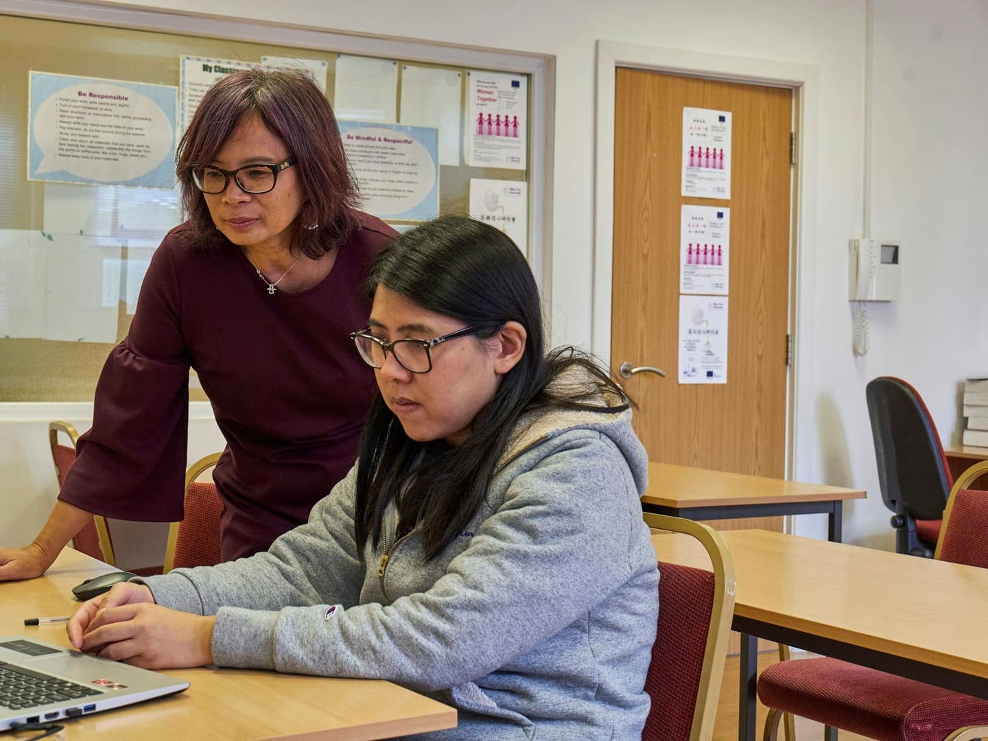 Une enseignante se penche sur l'écran d'une étudiante en salle de classe